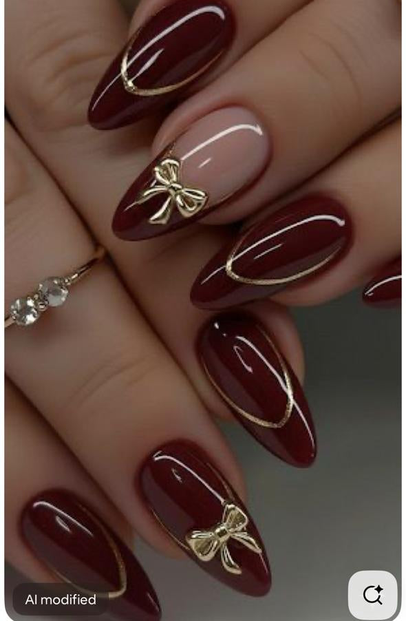 Maroon nails with gold bows and accents on a hand, displayed on a smartphone screen.